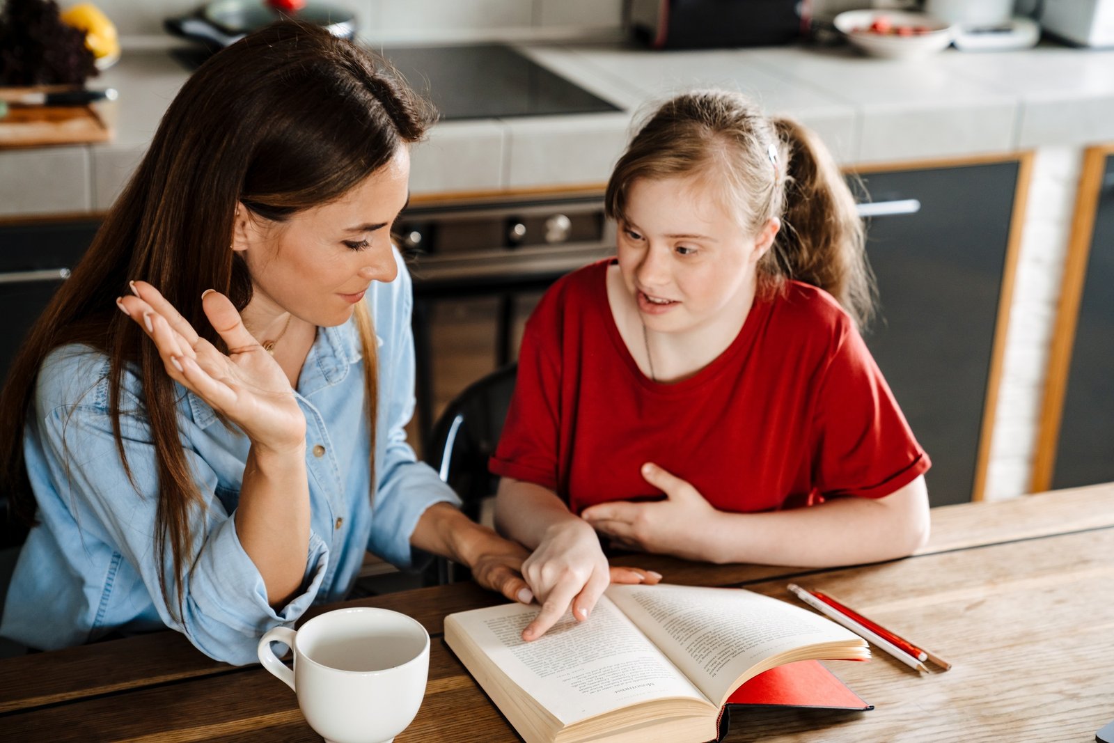 White woman helping her daughter with down syndrome reading book